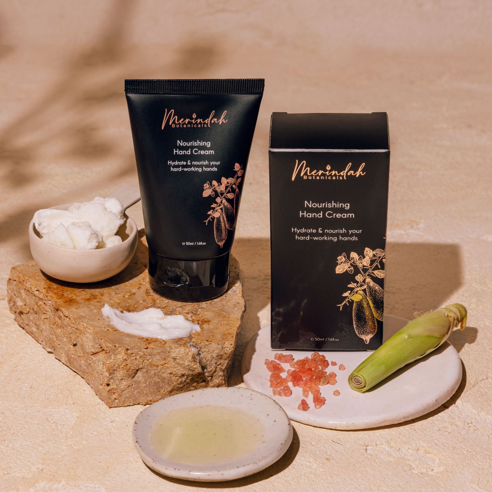 A tube of nourishing hand cream displayed alongside its packaging, with a small bowl with shea butter and a Australian Finger Lime Caviar, all set against a neutral background.