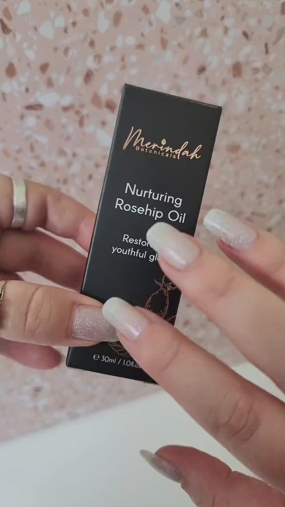 Woman hands showing Merindah Botanicals rose hip seed oil in black packaging and out of packaging applied to hand.