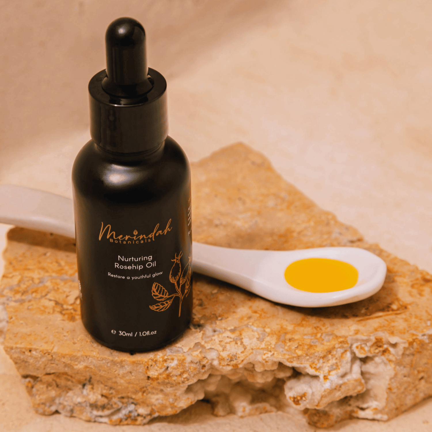 Bottle of Merindah Botanicals rosehip oil for face on stone with spoon filled next to it.