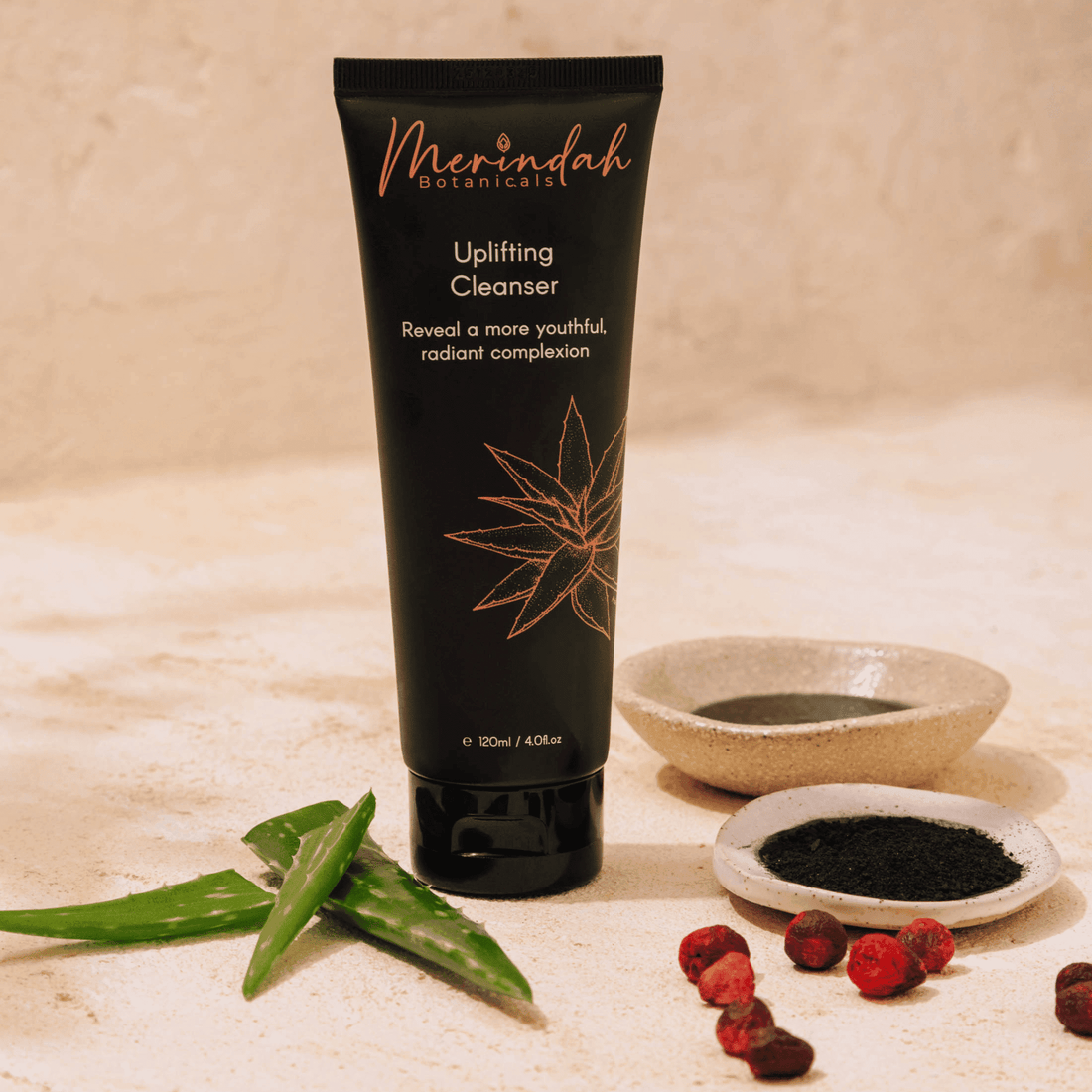 A tube of Uplifting Cleanser by Merindah Botanicals, displayed with aloe vera leaves and berries to highlight its organic feel. This natural cleanser with botanicals features activated charcoal and meadowfoam oil for gentle, effective cleansing.