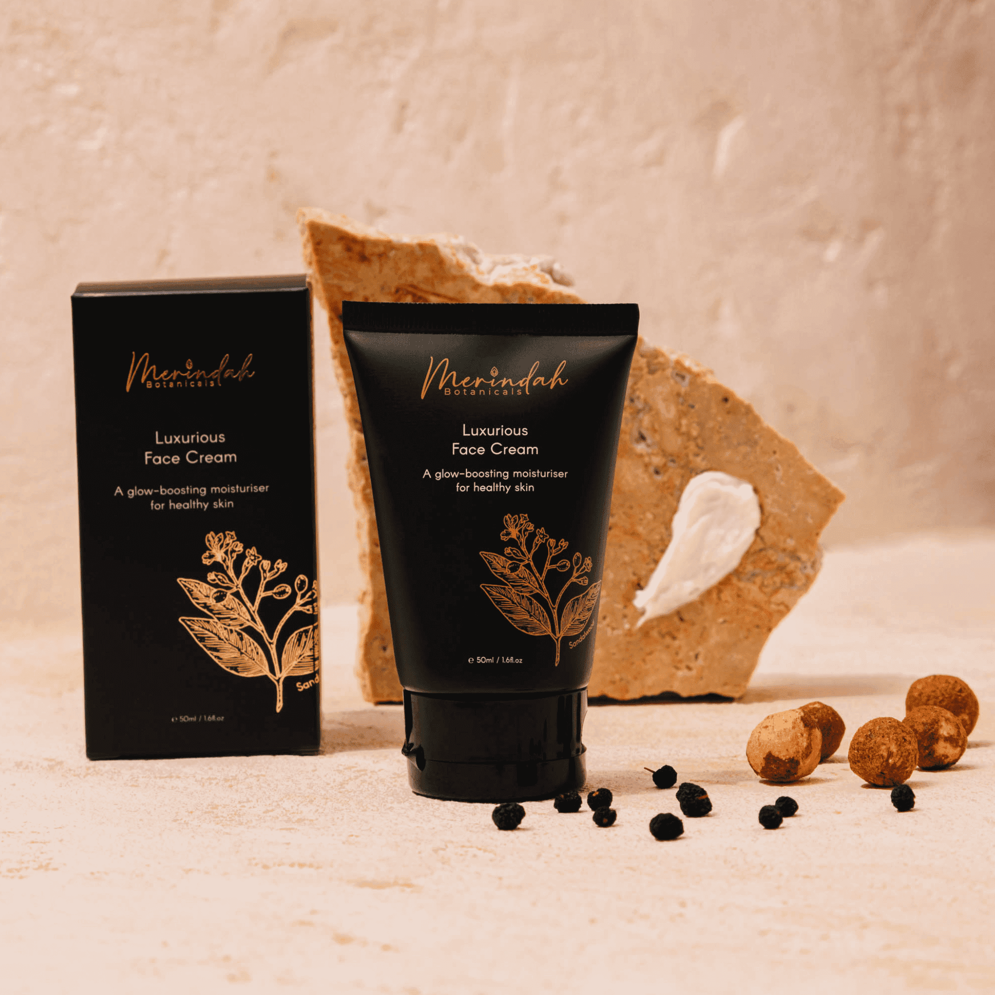 A luxurious face cream by Merinah Botanicals displayed in a black tube with golden botanical print, accompanied by its packaging box, with natural ingredients like nuts and berries scattered around, against a neutral backdrop.